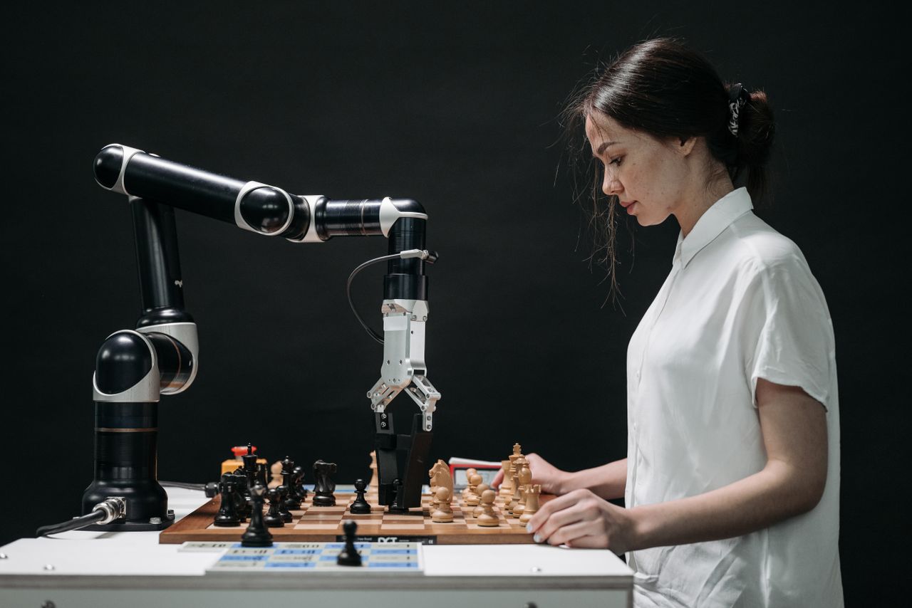heros-img A robot and woman engage in chess, showcasing technology and strategic thinking.